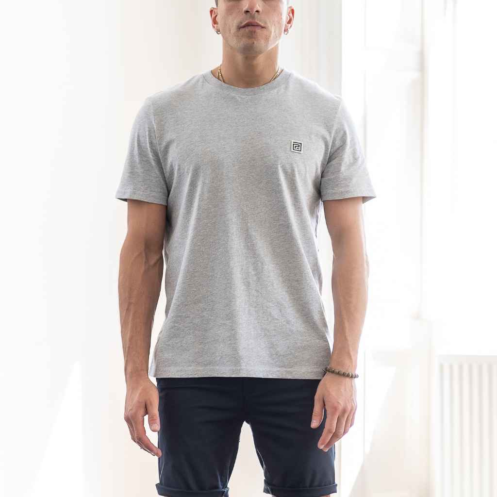 A person wearing a paradaiza gray heather classic crewneck t-shirt and dark shorts standing indoors.
