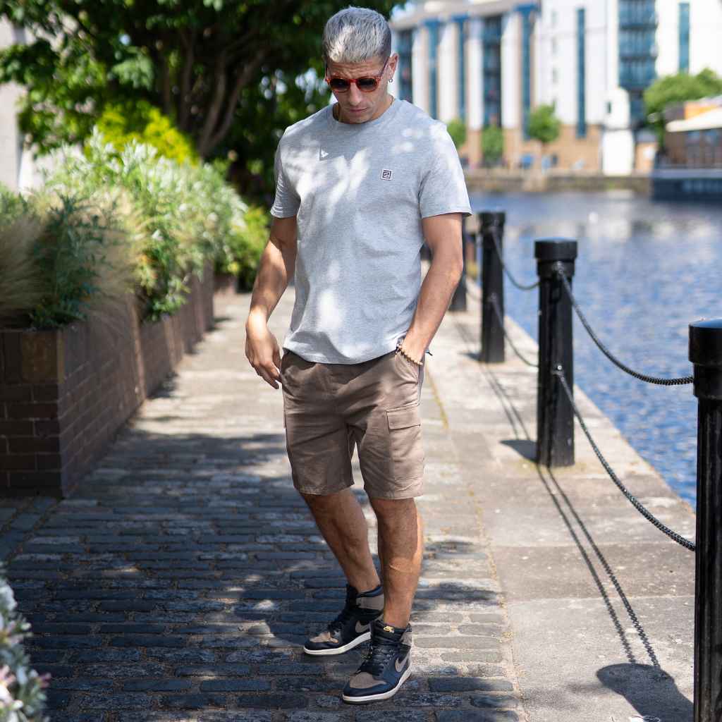 A person wearing a paradaiza gray heather classic crewneck t-shirt and light shorts standing outdoors.