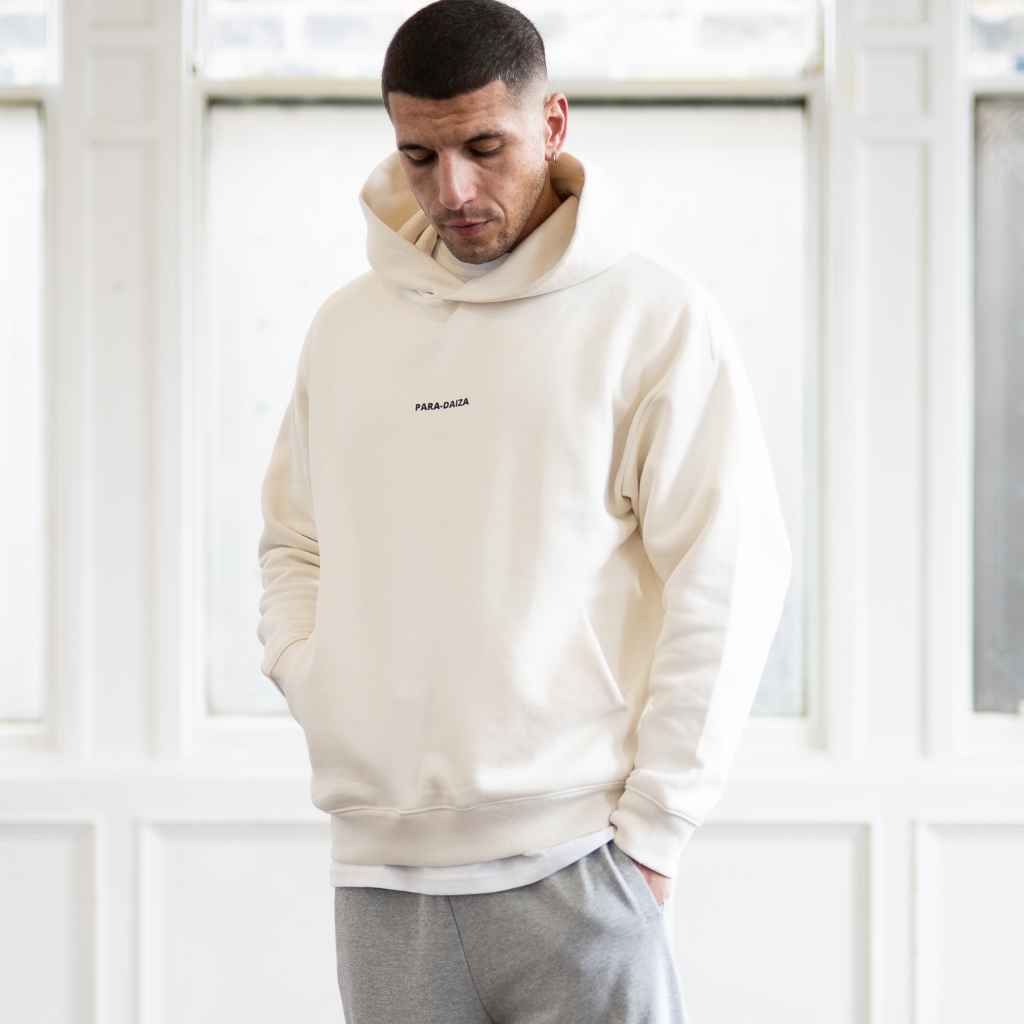 A male model wearing an oversized Paradaiza hooded sweatshirt in off white color, with the brand name 'PARA-DAIZA' visible on the front.