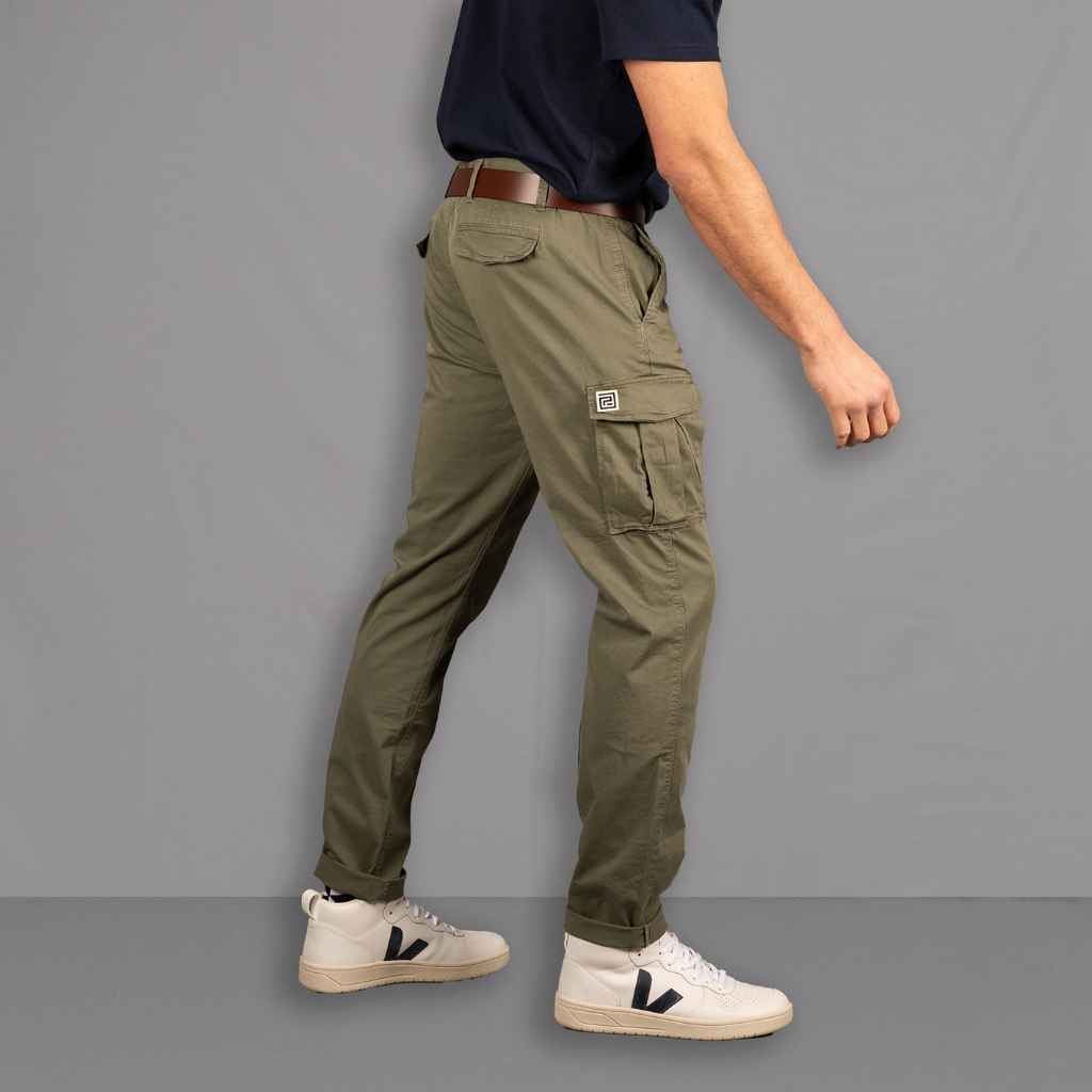 A person standing on a wooden floor wearing PARADAIZA olive green cargo pants with a belt loop, chain stitch detail, and multiple pockets, paired with a white shirt and white sneakers.