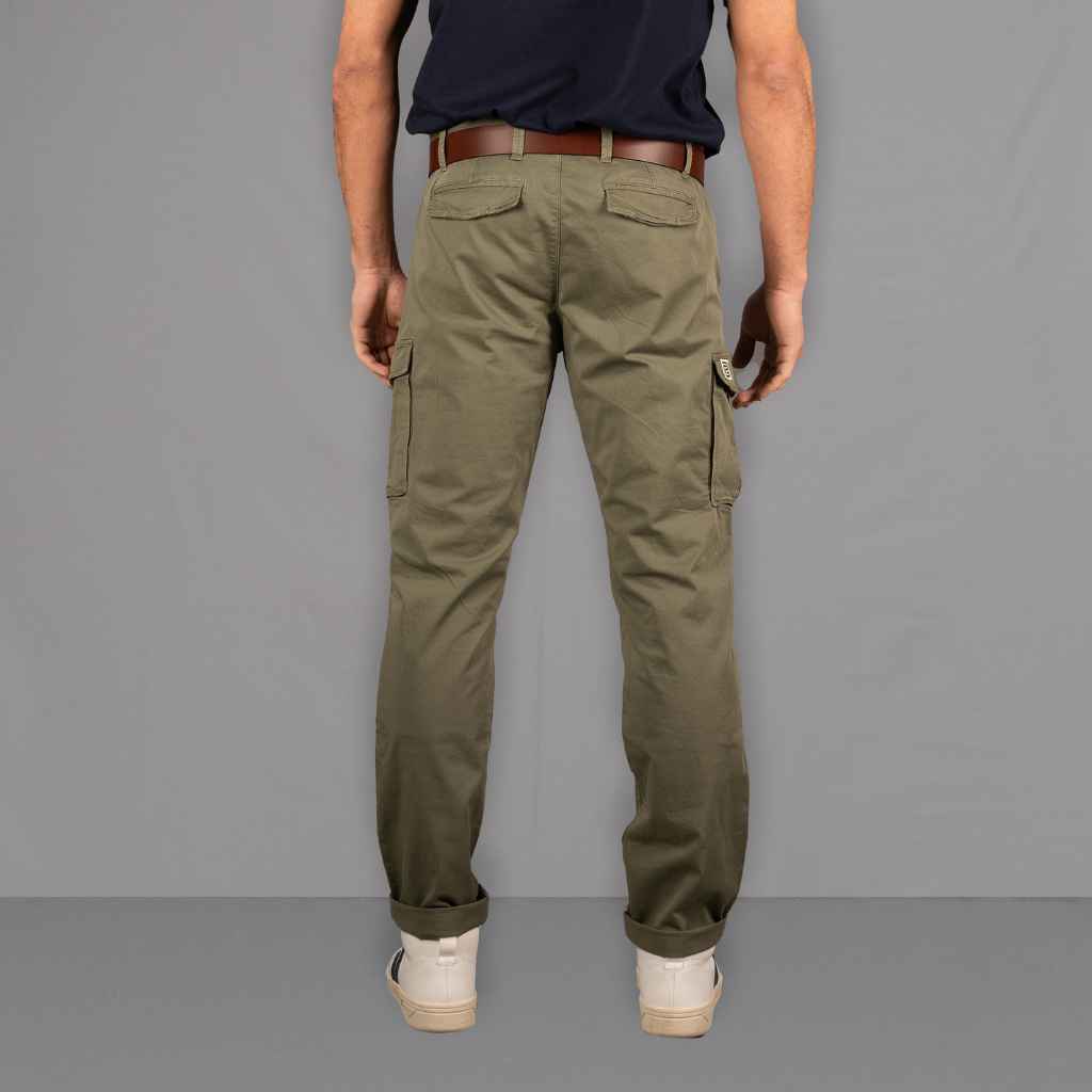 A person standing on a wooden floor wearing PARADAIZA olive green cargo pants with a belt loop, chain stitch detail, and multiple pockets, paired with a white shirt and white sneakers.