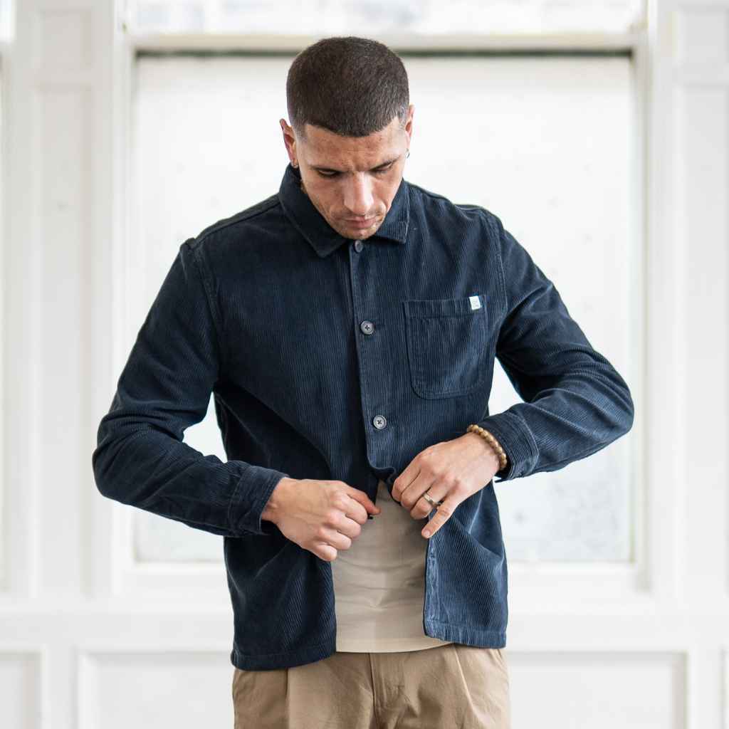 A male model wearing a paradaiza navy-colored corduroy overshirt with a collar, patch chest pocket, and buttons down the front, paired with beige pants.