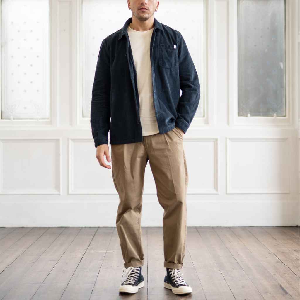 A male model wearing a paradaiza navy-colored corduroy overshirt with a collar, patch chest pocket, and buttons down the front, paired with beige pants.