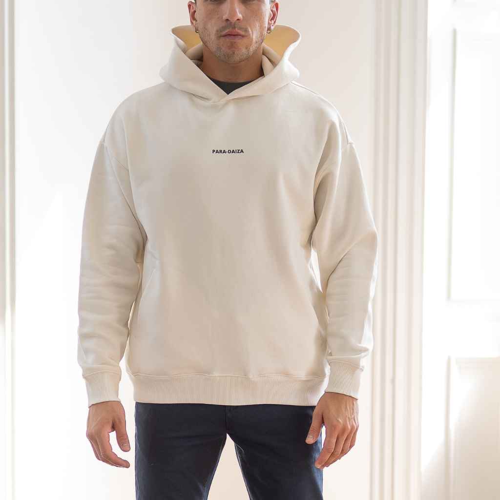 A male model wearing an oversized Paradaiza hooded sweatshirt in off white color, with the brand name 'PARA-DAIZA' visible on the front.