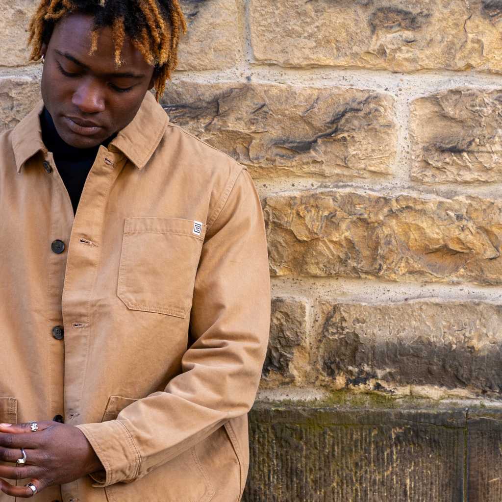 Man wearing a Tan paradaiza worker jacket standing against a stone wall