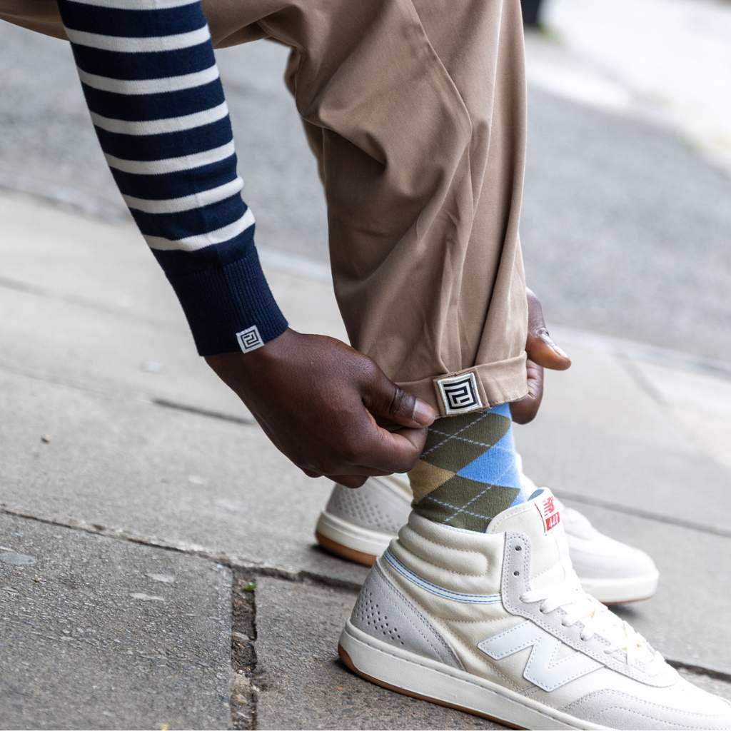 Person wearing white new balance sneakers, paradaiza pinch chinos beige pants, and patterned socks on a sidewalk.