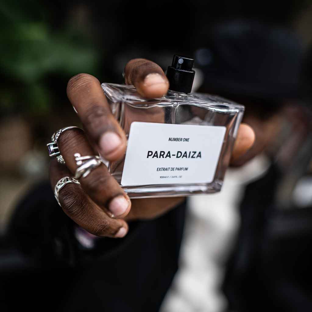 A person holding a bottle of perfume labeled 'PARA-DAIZA' with a blurred background.