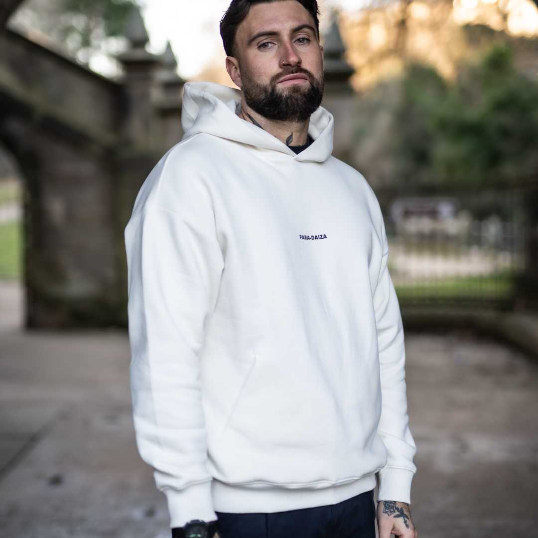 A male model wearing an oversized Paradaiza hooded sweatshirt in off white color, with the brand name 'PARA-DAIZA' visible on the front.