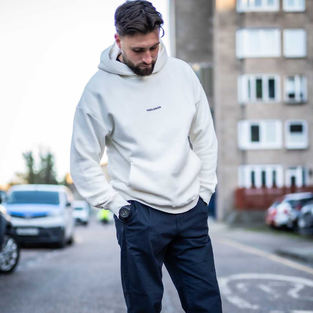 A male model wearing an oversized Paradaiza hooded sweatshirt in off white color, with the brand name 'PARA-DAIZA' visible on the front.