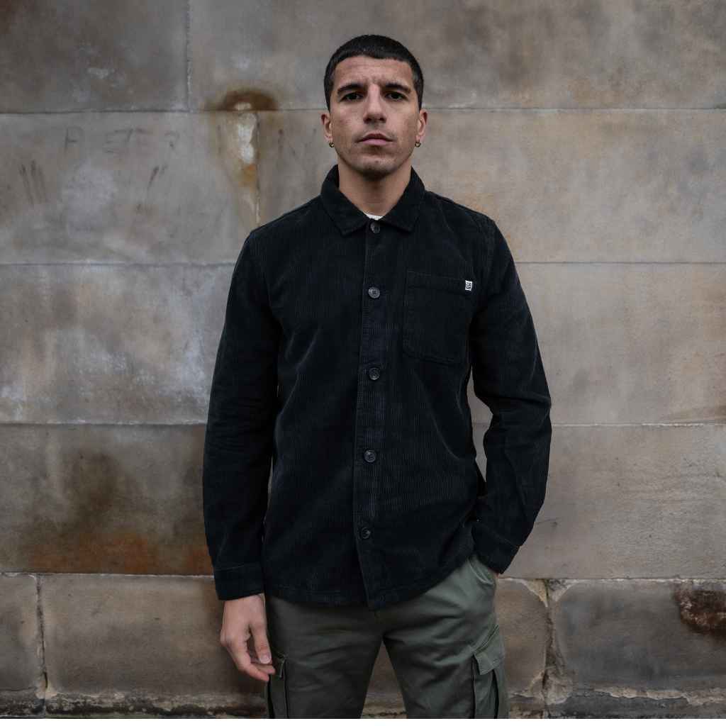 A male model wearing a para daiza long-sleeved black overshirt with a collar, patch chest pocket, and buttons down the front.