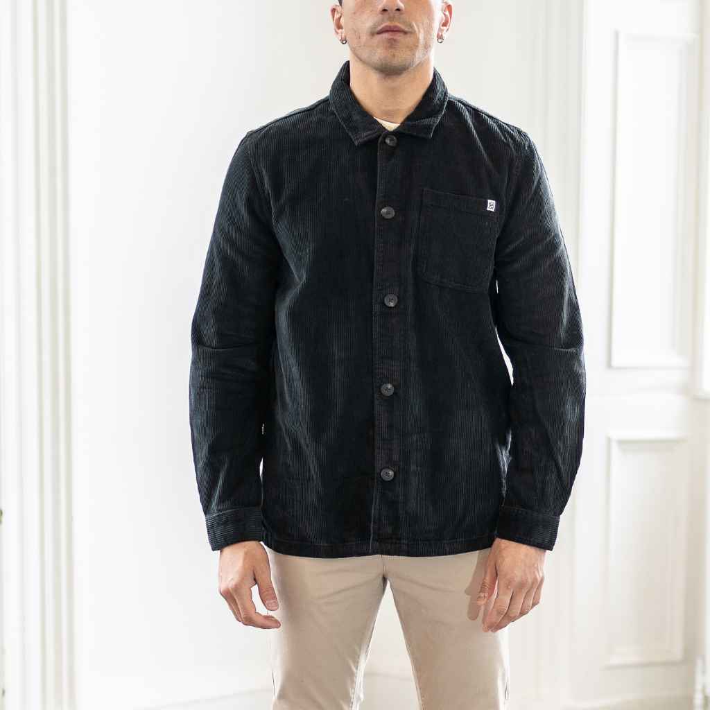 A male model wearing a para daiza long-sleeved black overshirt with a collar, patch chest pocket, and buttons down the front.