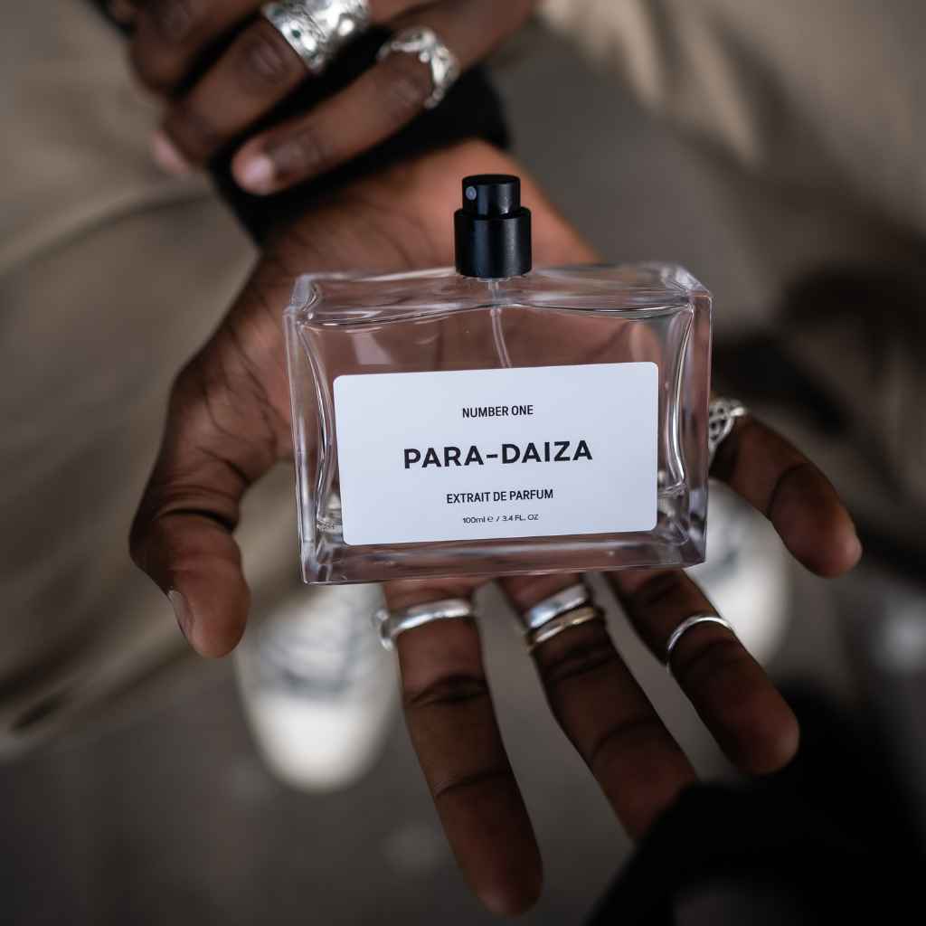 A person holding a bottle of perfume labeled 'PARA-DAIZA' with a blurred background.