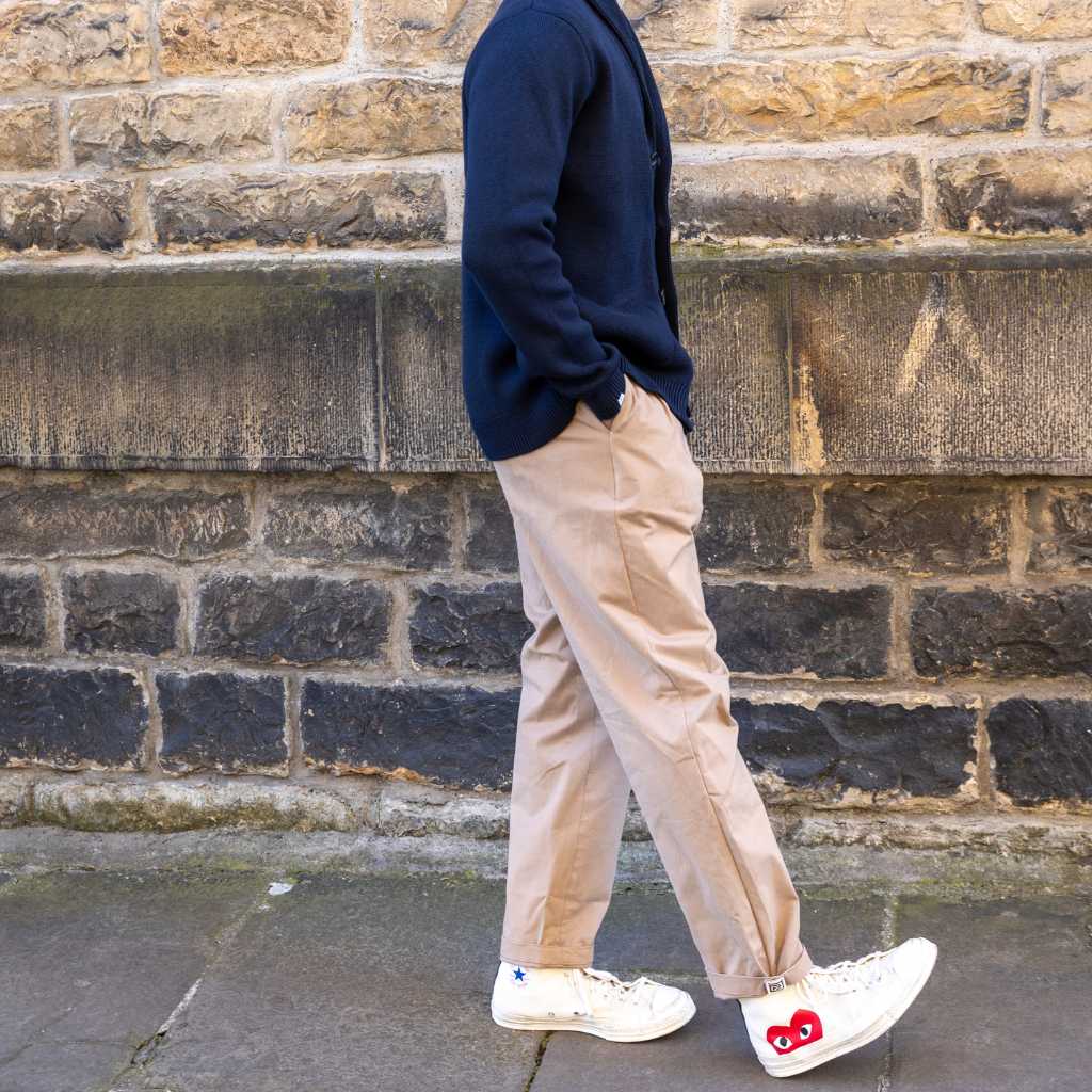 Person wearing paradaiza pinch chinos in beige and white sneakers with a red heart design against a brick wall.
