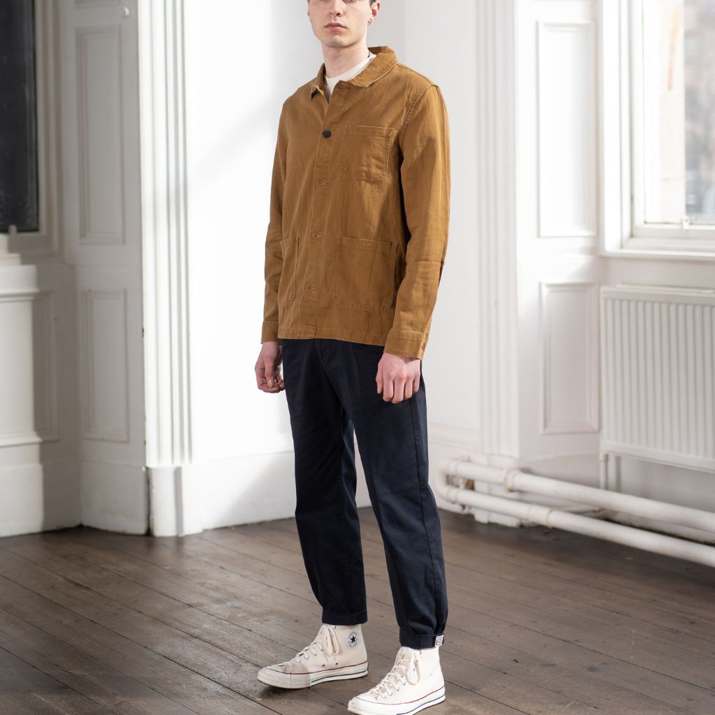 A person wearing a Paradaiza brown worker jacket with buttons, standing on wooden floor.