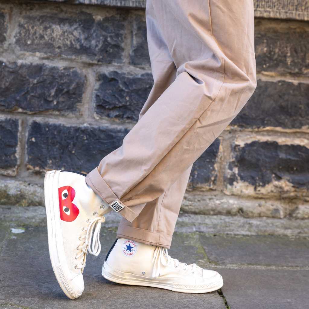 Person wearing paradaiza pinch chinos in beige and white sneakers with a red heart design against a brick wall.