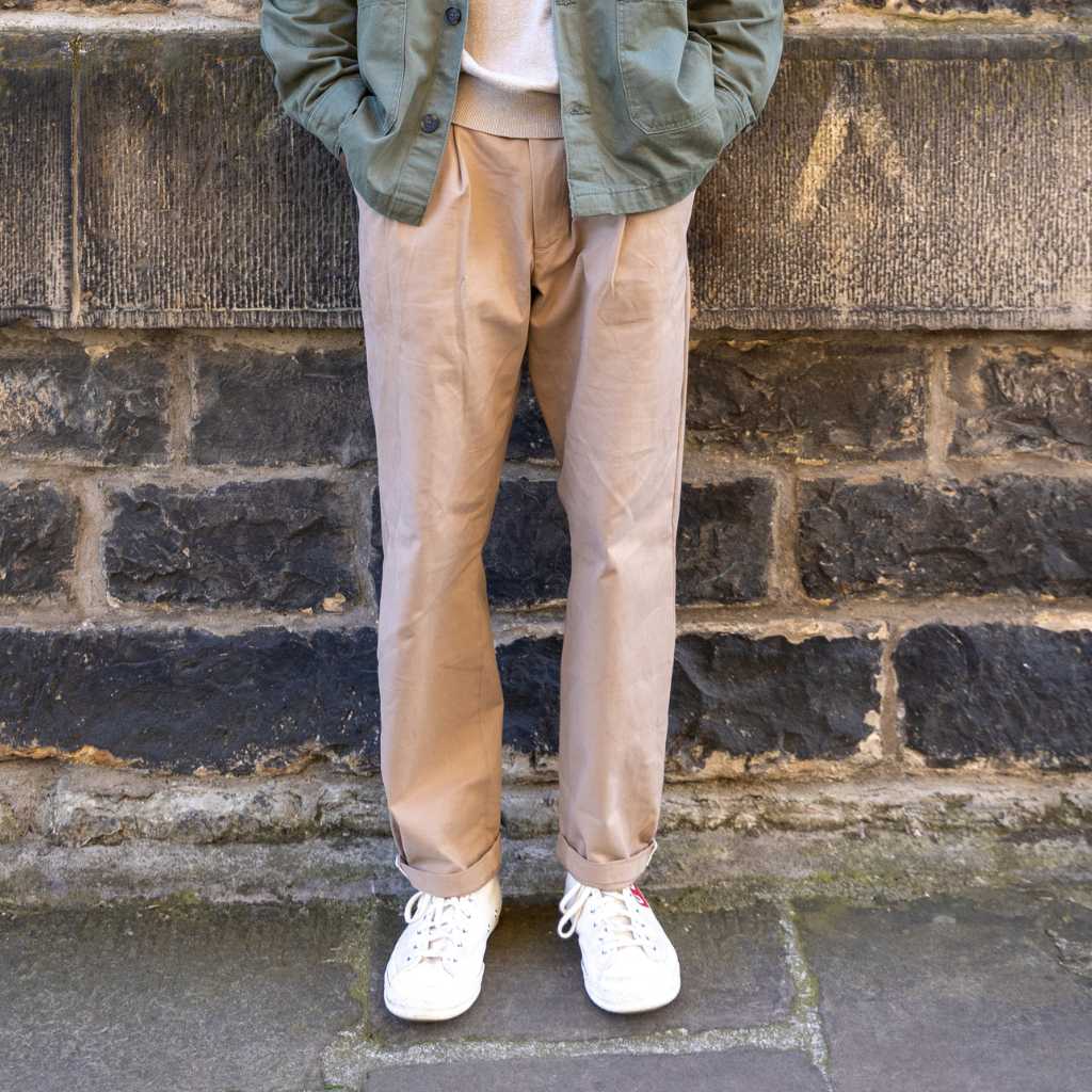 Person wearing paradaiza pinch chinos in beige and white sneakers with a red heart design against a brick wall.