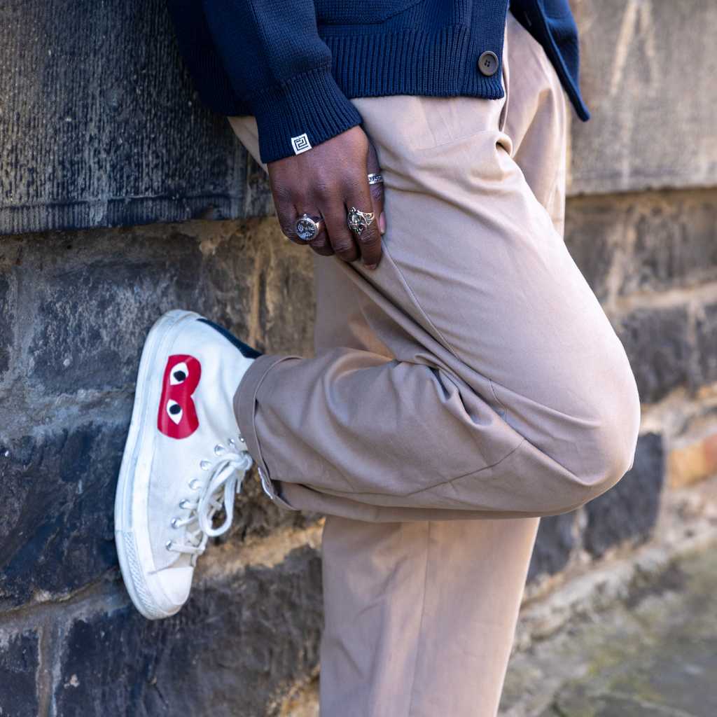 Person wearing paradaiza pinch chinos in beige and white sneakers with a red heart design against a brick wall.