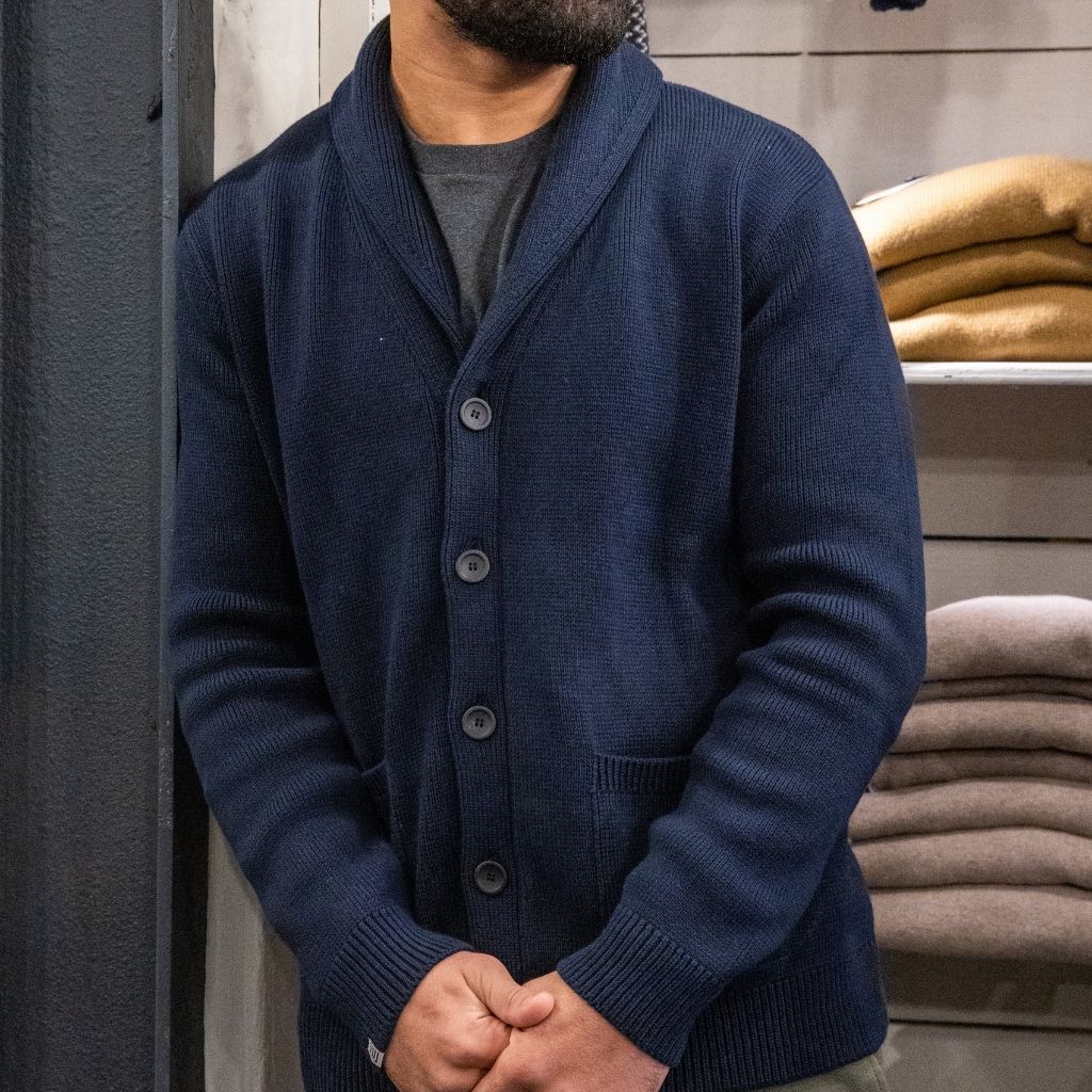 Man wearing a navy paradaiza cardigan over a red shirt against a gray background