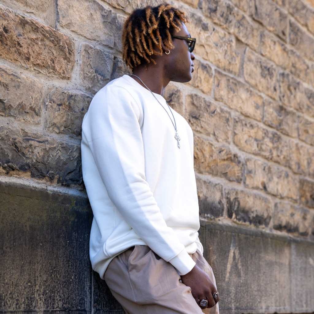 Man wearing a ivory paradaiza sweater and sunglasses against a stone wall