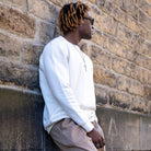 Man wearing a ivory paradaiza sweater and sunglasses against a stone wall