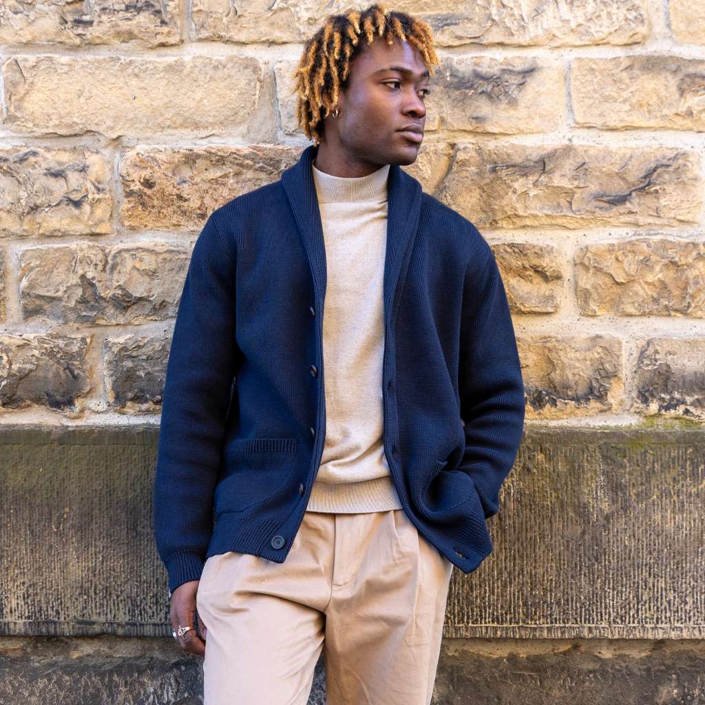 Person wearing a paradaiza navy blue cardigan over a beige shirt against a stone wall.