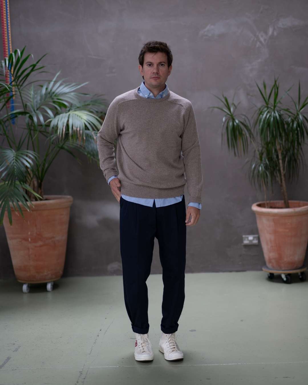 Man wearing a paradaiza brown sweater over a light blue shirt against a gray background