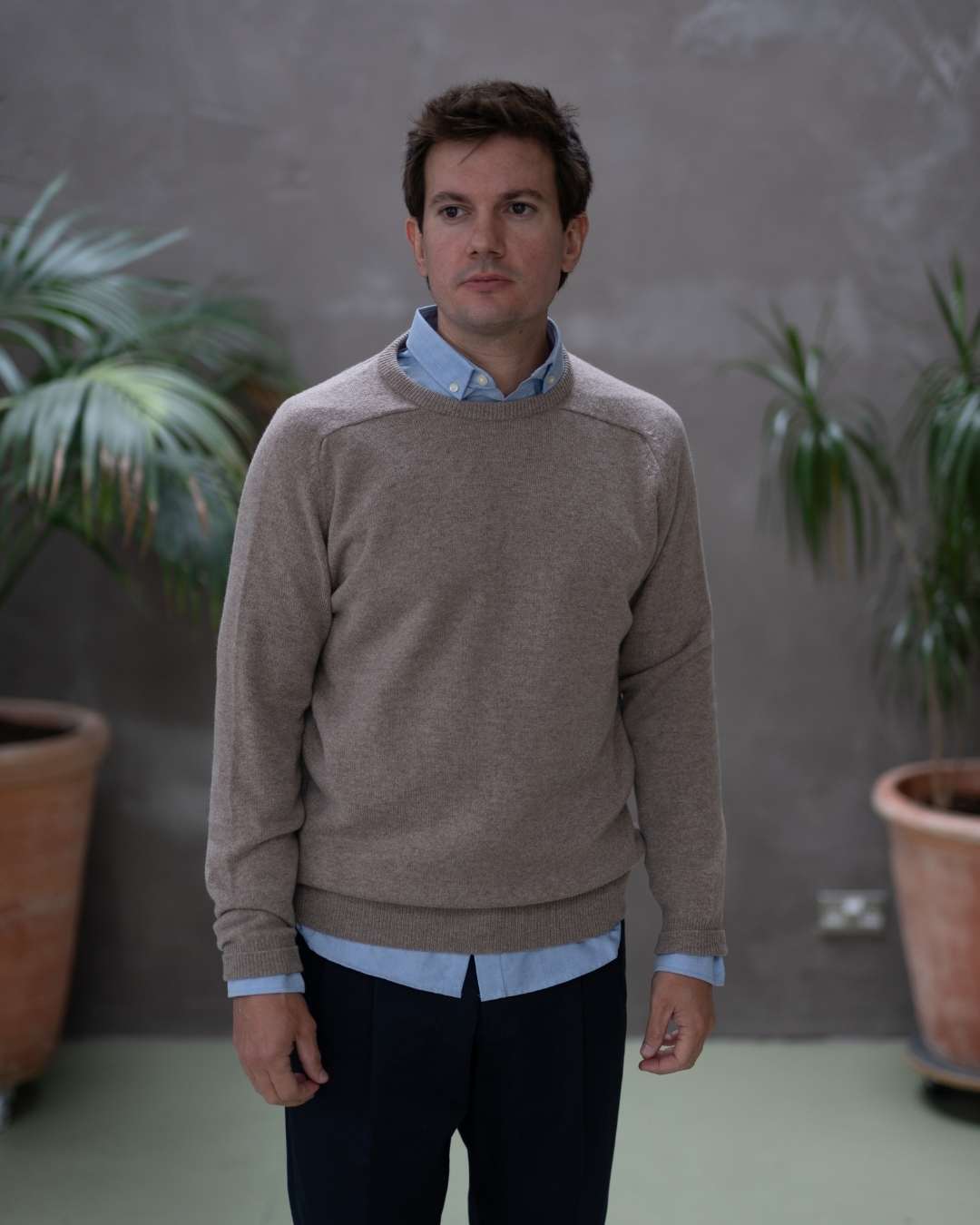 Man wearing a paradaiza brown sweater over a light blue shirt against a gray background