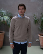 Man wearing a paradaiza brown sweater over a light blue shirt against a gray background