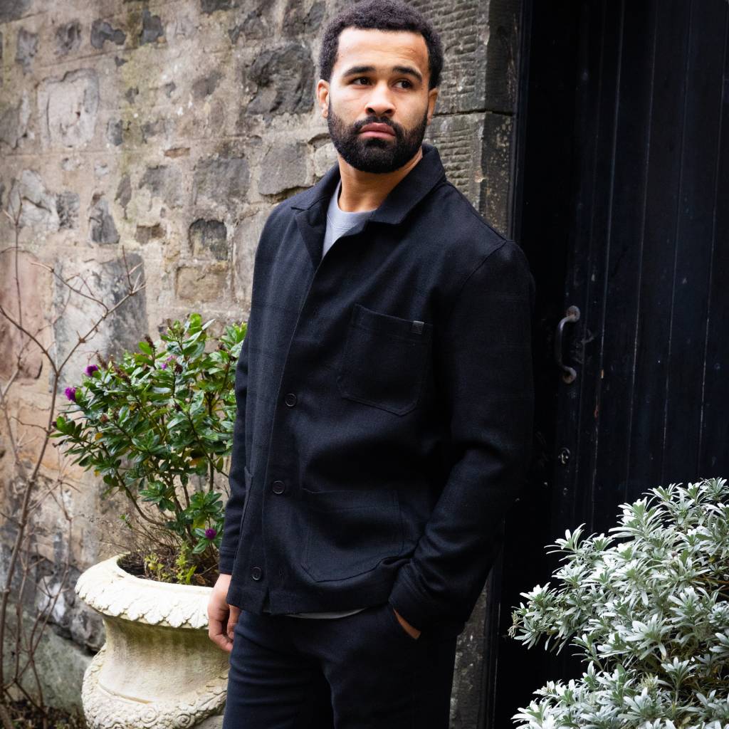 Man wearing a  paradaiza wool worker black jacket standing in front of a stone wall in circus lane stockbridge 
