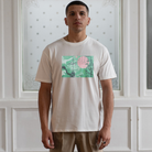 Man wearing a paradaiza white t-shirt with a graphic design in front of a white paneled wall.