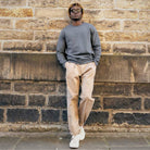 Man leaning against a stone wall wearing a PARADAIZA grey sweater and beige pants.
