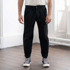 Person wearing black paradaiza pinch chinos pants and high-top sneakers in a room with wooden floor and white walls.
