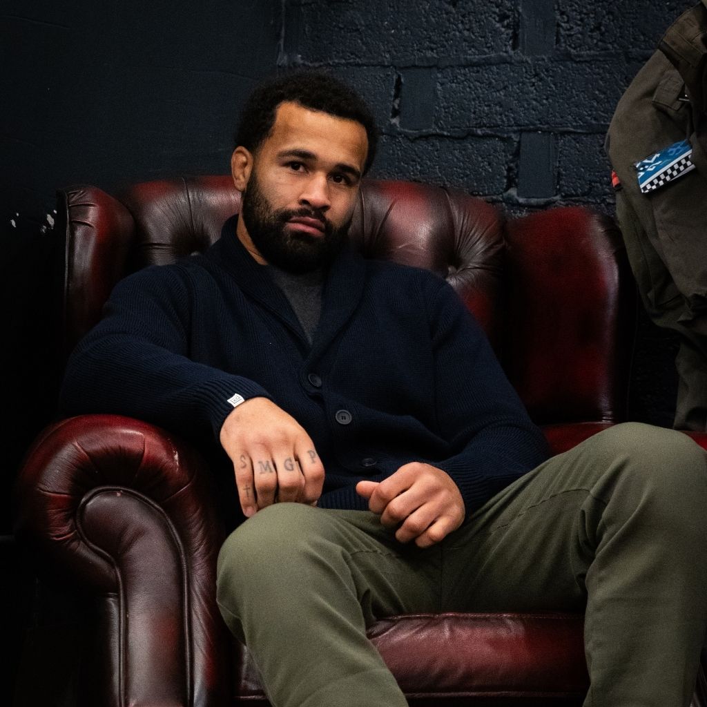 Man sitting on a leather chair against a dark brick wall wearing paradaiza