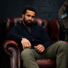 Man sitting on a leather chair against a dark brick wall wearing paradaiza
