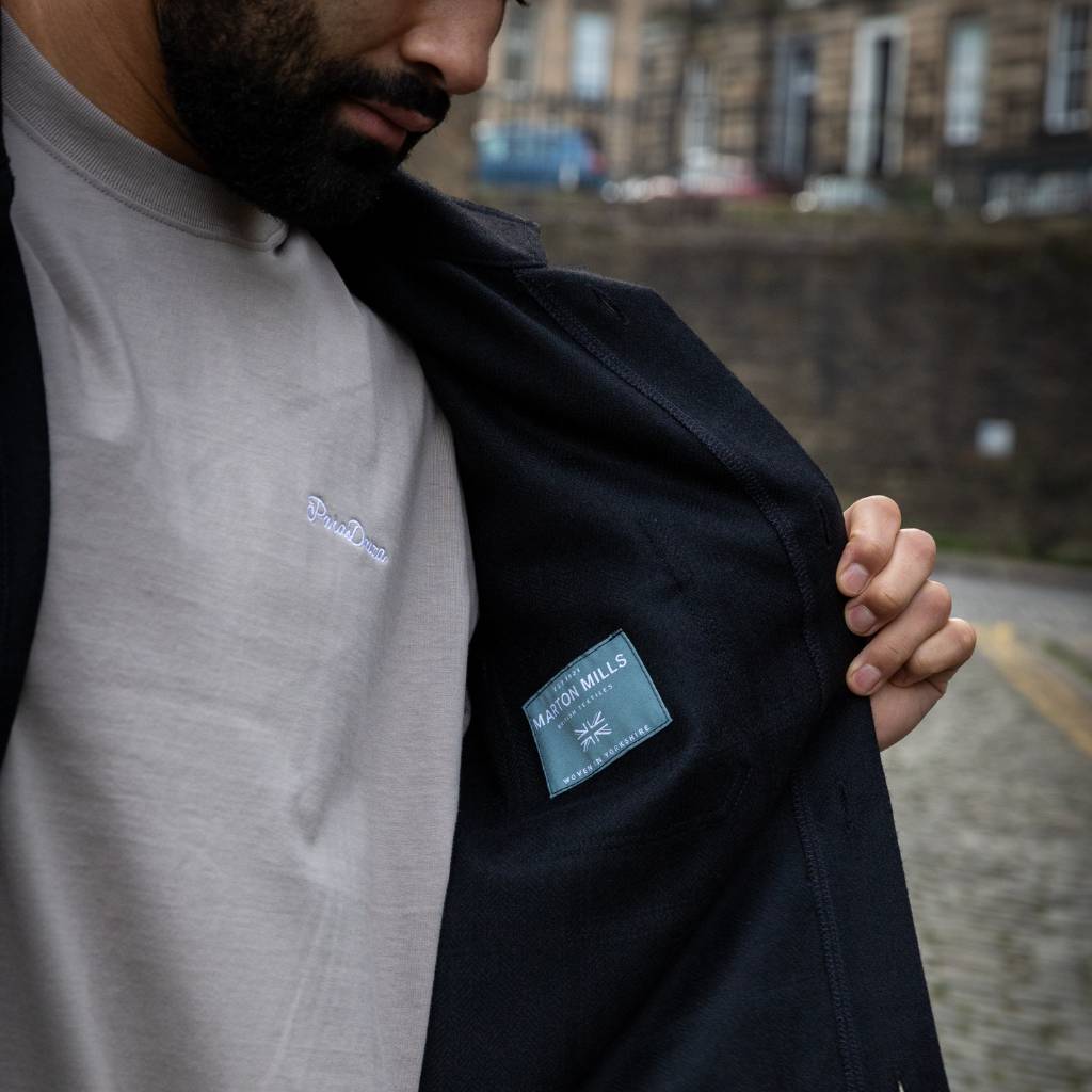 Man wearing a  paradaiza wool worker black jacket standing in front of a stone wall in circus lane stockbridge 