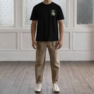 Person wearing a black paradaiza  t-shirt with a forest design on the back, standing against a white paneled wall.