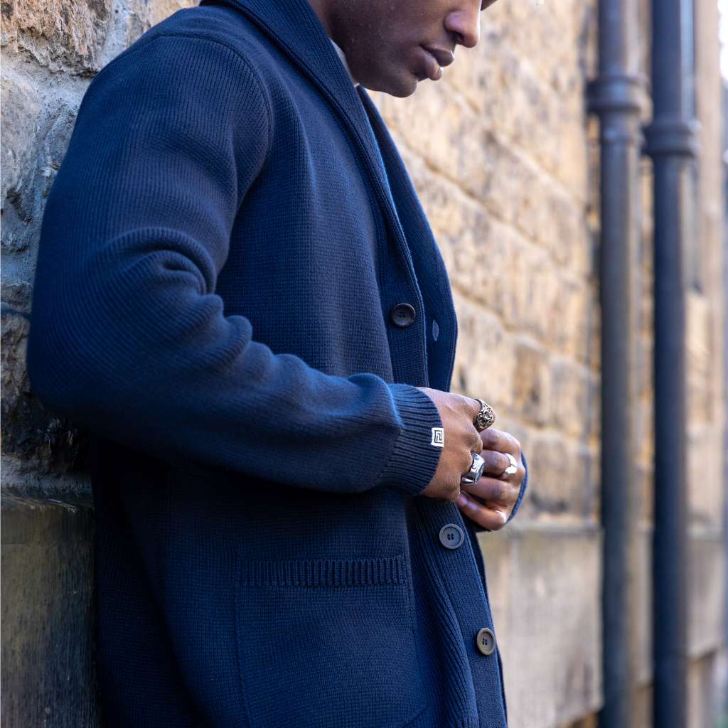 Person wearing a paradaiza navy blue cardigan over a beige shirt against a stone wall.
