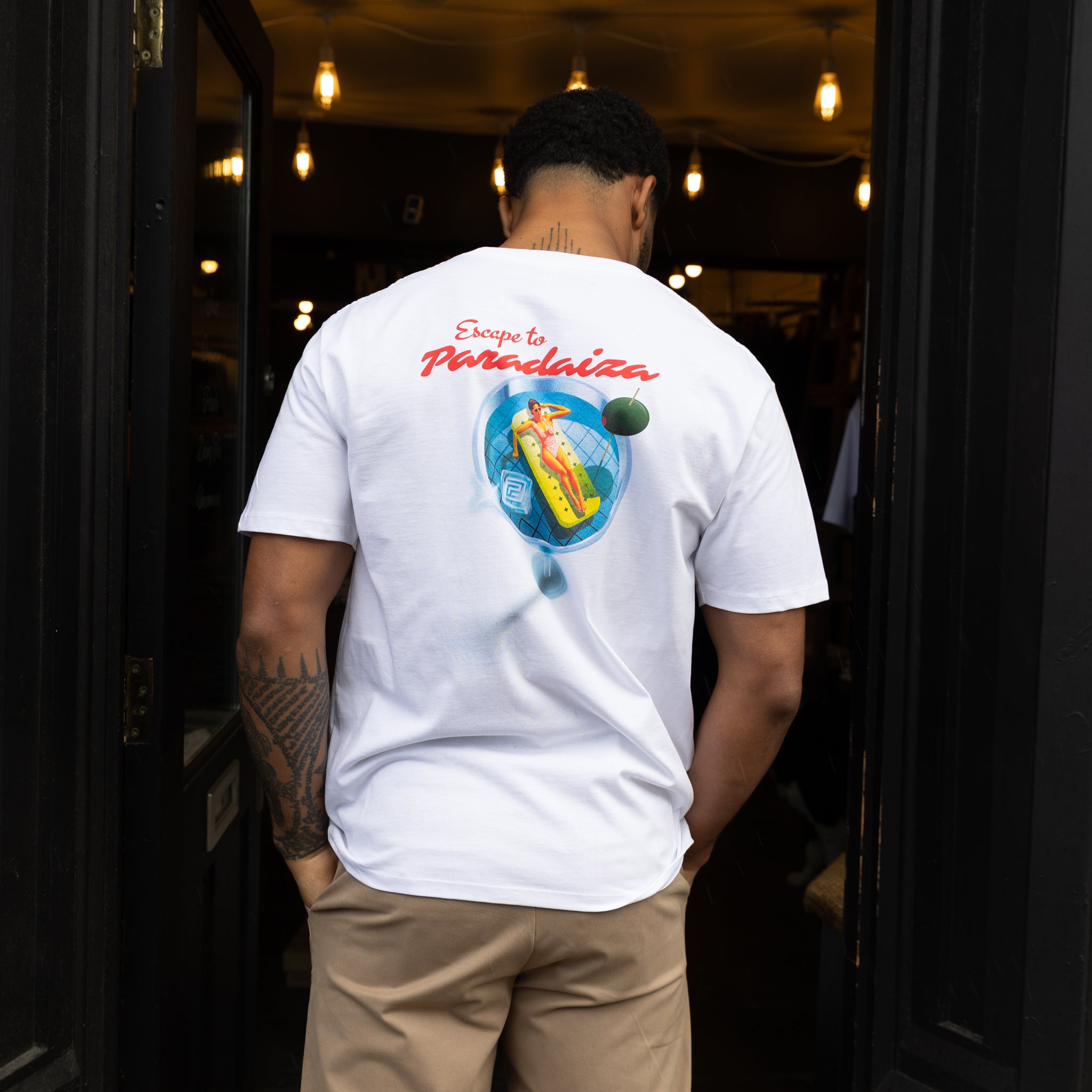 Person wearing paradaiza  white t-shirt with a colorful graphic on the back, standing in a doorway of paradaiza stockbridge 