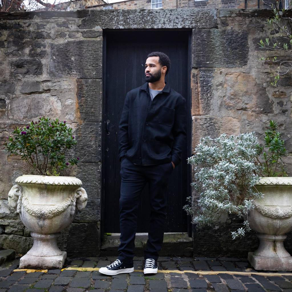Man wearing a  paradaiza wool worker black jacket standing in front of a stone wall in circus lane stockbridge 