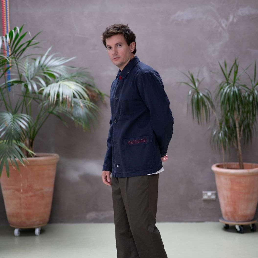 Model wearing a  paradaiza dark blue worker jacket with patterned accents and sashiko stitching  in a studio.