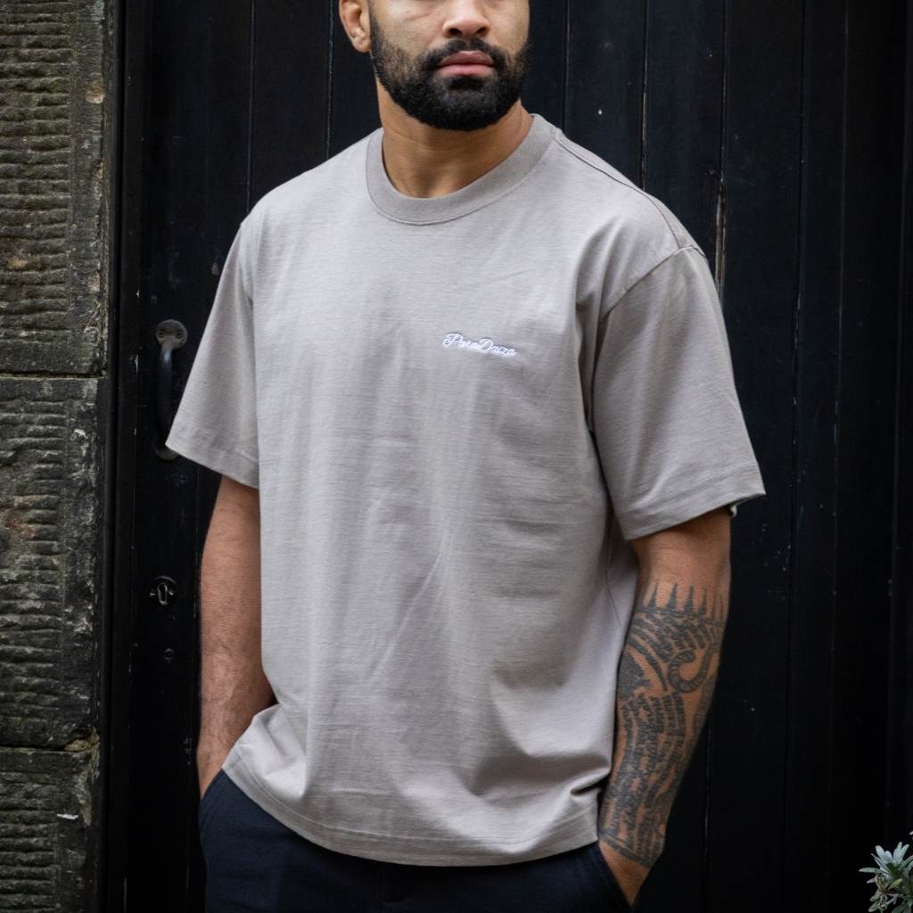 Beige paradaiza  t-shirt with a logo on the back against a dark background