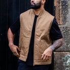 Man wearing a paradaiza tan vest over a black shirt standing in front of a dark door.