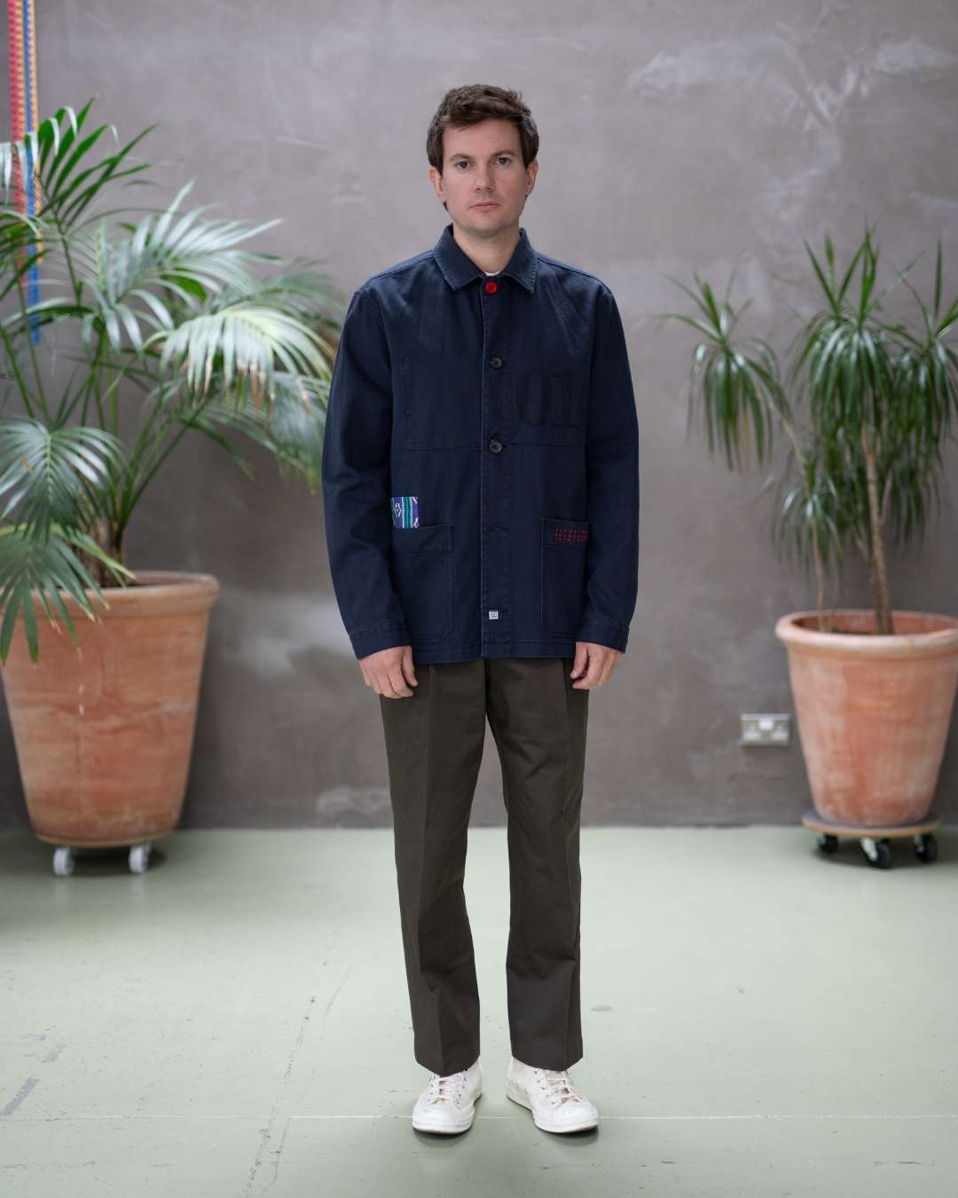 Model wearing a  paradaiza dark blue worker jacket with patterned accents and sashiko stitching  wearing khaki chinos  in a studio.