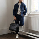 Man holding a  paradaiza black leather weekend bag in a room with a window .