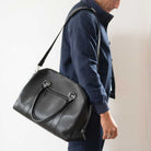 Man holding a  paradaiza black leather weekend bag in a room with a window .