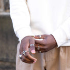 Close-up of hands with multiple rings on fingers, wearing a white outfit.