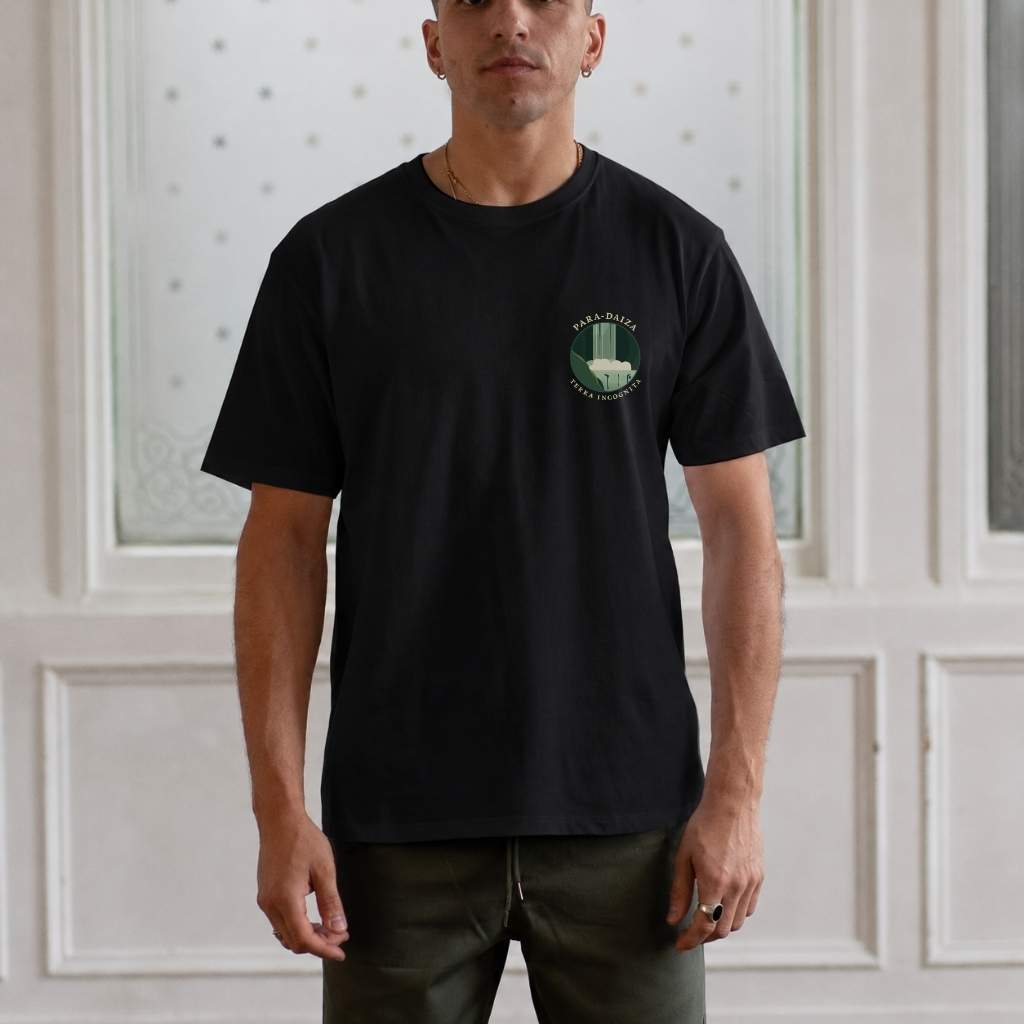 Man wearing a paradaiza  black t-shirt with a logo against a white paneled wall.