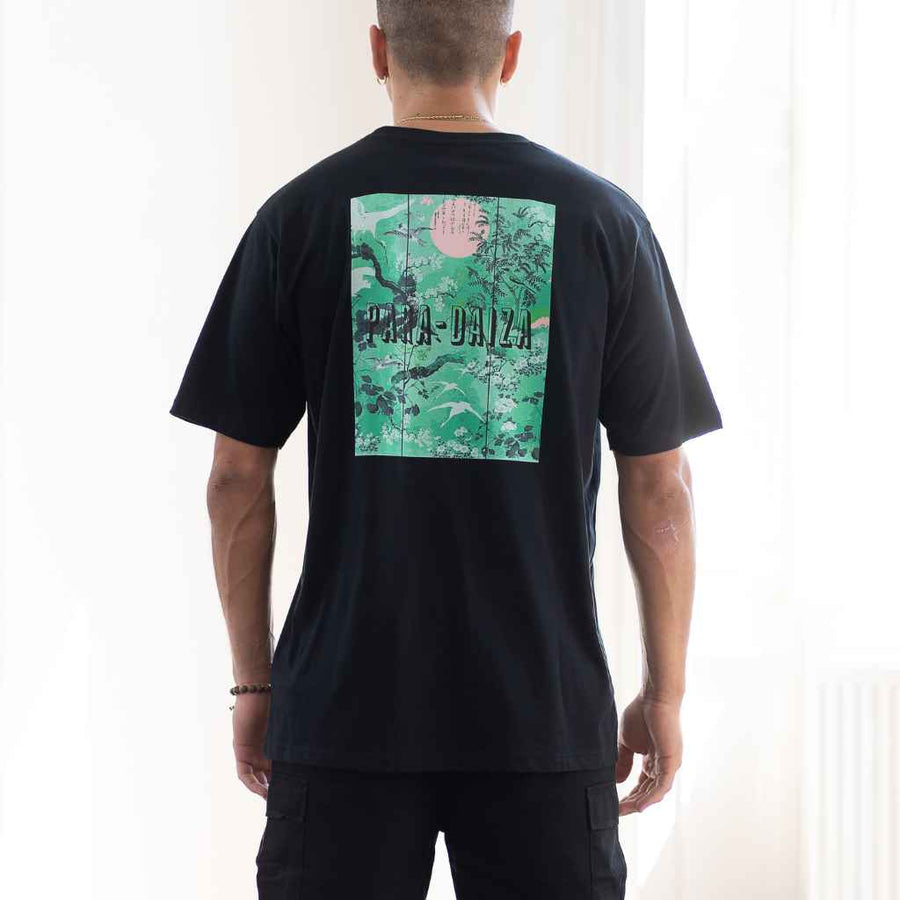 A person wearing a para daiza black oversized t-shirt with a graphic print in the center, viewed from the back.