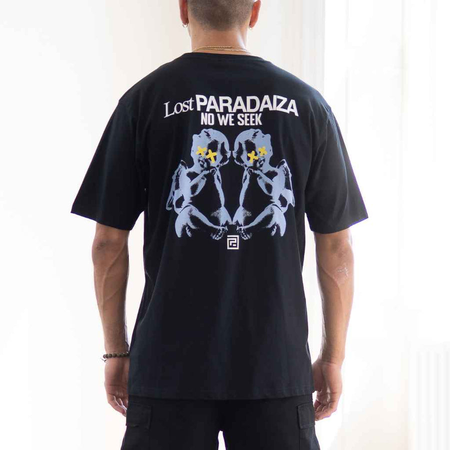 A person wearing a paradaiza  black oversized t-shirt with a graphic print on the back, predominantly featuring a cherub and the text 'Lost PARADAIZA NO WE SEEK'.