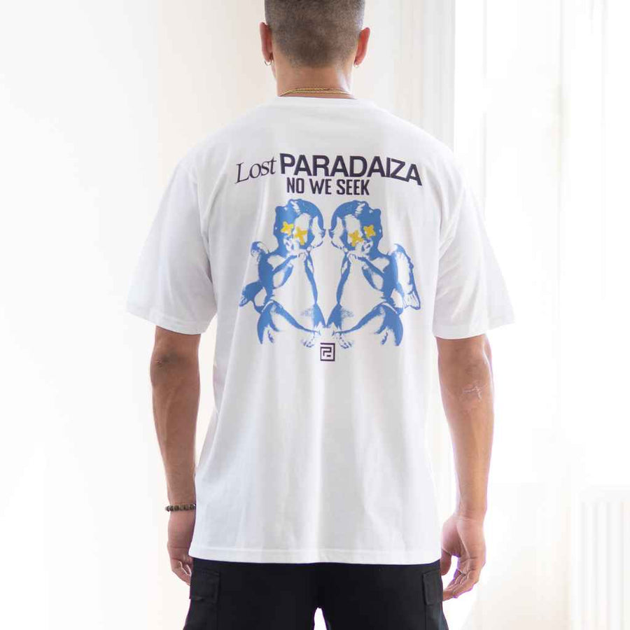 A person wearing a para daiza white oversized t-shirt with a graphic print on the back, text reads 'Lost PARADAIZA NO WE SEEK' with a floral and cherub design.